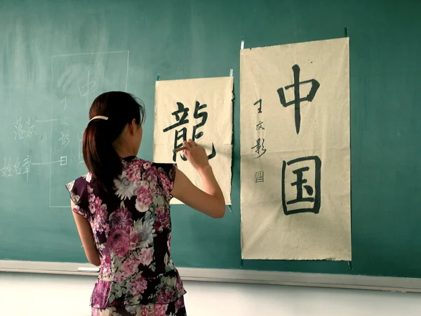 Chinese calligraphy teacher demonstrating brush technique in a classroom