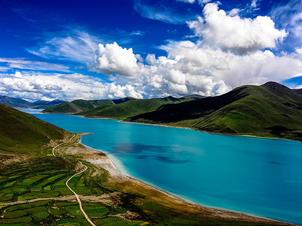 Turquoise Namtso lake and green highland beneath white clouds in Tibet