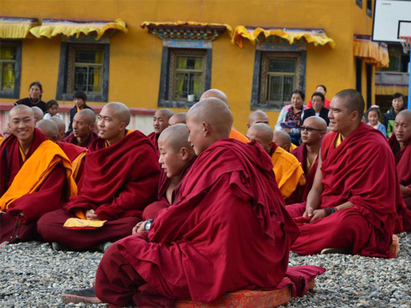 Tibetan Buddhist monks seated together outside a monastery building Tibetan Buddhist monks seated together outside a monastery building